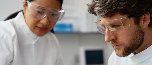 Two scientists working together  Two scientists wearing lab coats and goggles working together